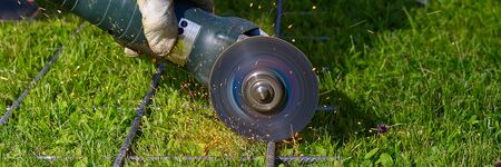 Cutting metal net with grinder on green grass. Sparks from contact materials. Worker outside, cut...