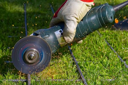 Cutting metal net with grinder on green grass. Sparks from contact materials. Worker outside, cut...