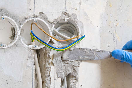 hidden installation of electrical wires for sockets to a concrete wall. The master is plastering the...