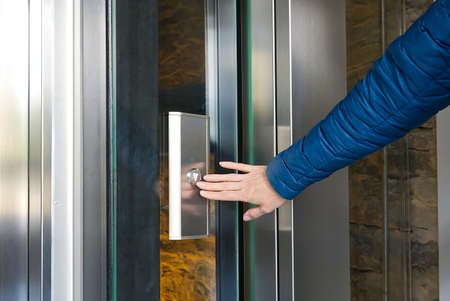 Woman pressing the button of the modern elevator made from glass