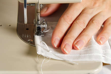 A woman works on a sewing machine. seamstress sews white curtains, close up view.