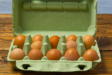 Dozen eggs in green cardboard package on wooden table closeup.