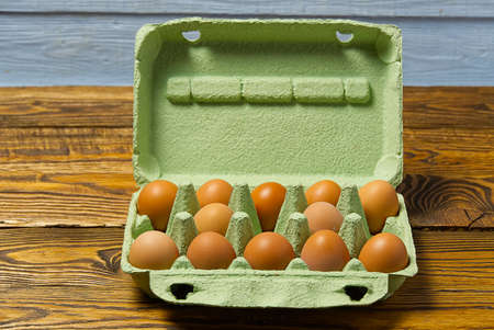 Dozen eggs in green cardboard package on wooden table closeup.