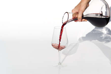 Sommelier pours red wine from decanter to wineglass on white background.