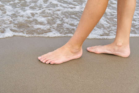 Close-up of childs legs walking on sand coast and sea water. Young girl legs on baltic sea beach. Teenager legs near sea line.の写真素材