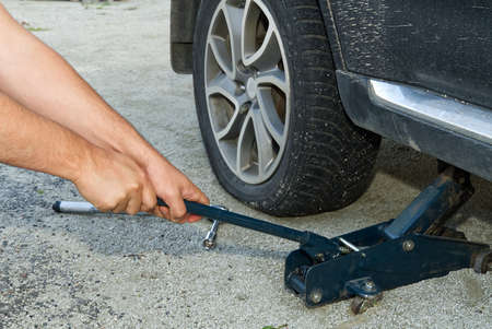 Man changing wheel. tire changer changing flat car tire. Mechanic hands unscrews a flat tire of a car raised on a jack Help on road or Tire help concept.の写真素材