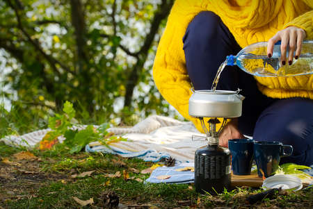 young beautiful girl in a yellow sweater makes coffee in the forest on a gas burner. Making coffee...