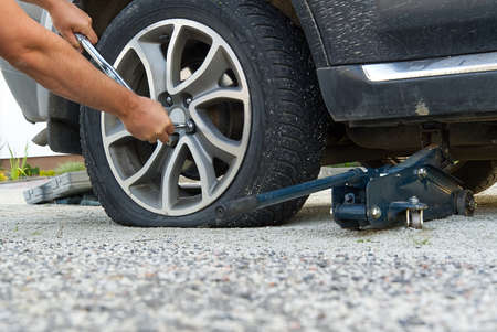 Man changing wheel. tire changer changing flat car tire. Mechanic hands unscrews a flat tire of a...