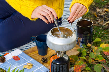 young beautiful girl in a yellow sweater makes coffee in the forest on a gas burner. Making coffee...