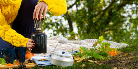 young beautiful girl in a yellow sweater makes coffee in the forest on a gas burner. Making coffee...