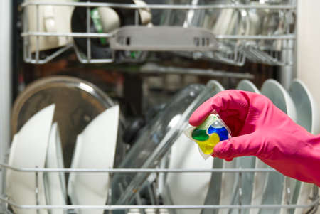 Dishwasher Detergents in hands. hands in pink golvs holds dishwasher gel capsules. Brilliant cleanliness. Capsule for the dishwasher.の写真素材