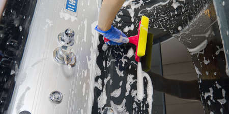 Cleaning of shower steam cabins from calcium deposits. Cleaning in the bathroom. hand in gloves with rag and detergent washing shower and glassの写真素材