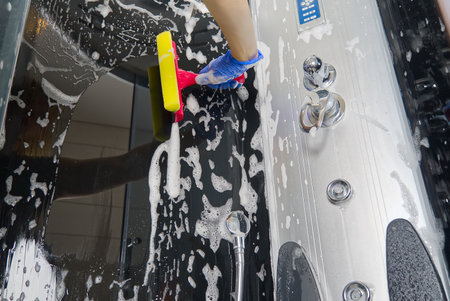 Cleaning of shower steam cabins from calcium deposits. Cleaning in the bathroom. hand in gloves with rag and detergent washing shower and glassの写真素材