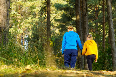 Mother with daughter hiking in autumn pine forest. Mom with daughter walking in nature on the forest...