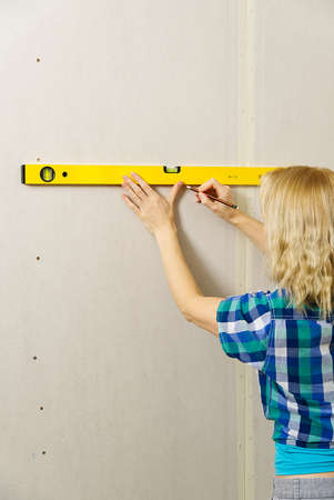 DIY blond young attractive woman using spirit level to work out measurements on plasterboard wall....