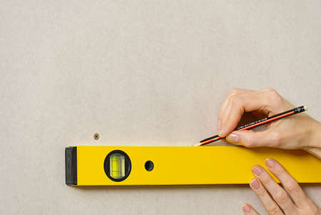 DIY blond young attractive woman using spirit level to work out measurements on plasterboard wall....