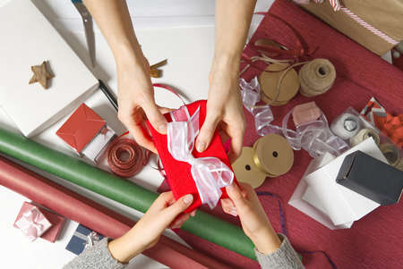 Close Up on hands women hands holding and giving red gift box with white ribbon to girl. Birthday,...