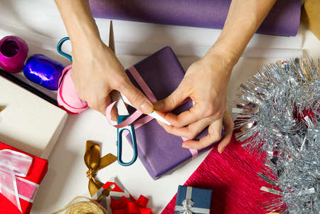 Woman wrapping christmas presents to violet packing paper. woman hands packing a christmas gift, diy...