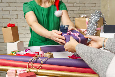 Female hands holding a small gift box wrapped in packing paper. To give and receive gifts from loved ones for christmas, valentines, birthday.の写真素材