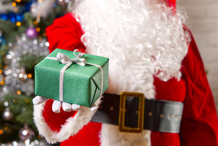 Santa Claus hands holds green gift box opposite christmas tree.の写真素材
