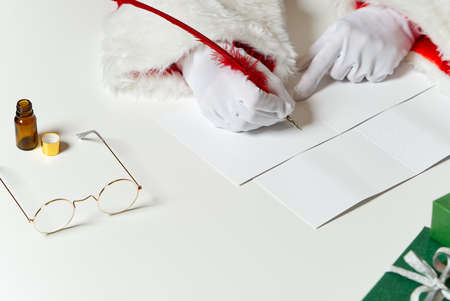 Costumed hands of Santa Claus writing a Christmas letter or greeting on a postcard. close upの写真素材