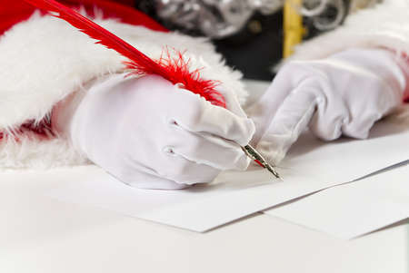 Costumed hands of Santa Claus writing a Christmas letter or greeting on a postcard. close upの写真素材