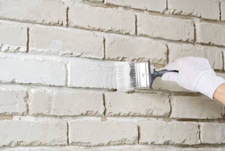 DIY wall repairing, Woman painting a white brick wall with a paint brushの写真素材