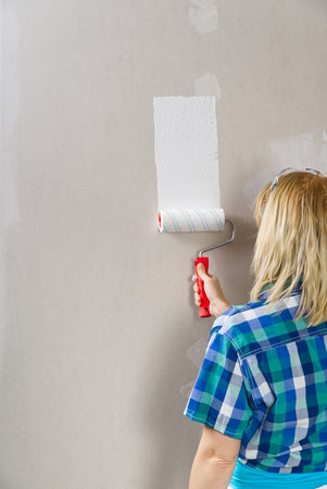 Woman painting cardboard wall to white. Home repairing, drywall painting with rollerの写真素材