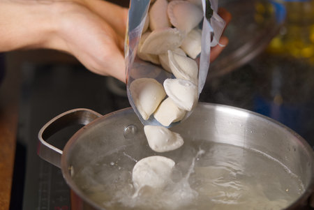 pouring dumplings from the packaging into pots of boiling water. Boiled dumplings in a panの写真素材
