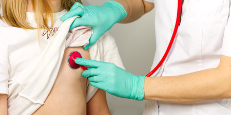 Little girl at the family doctor. lung area examined with stethoscope. Pediatrician checks the...