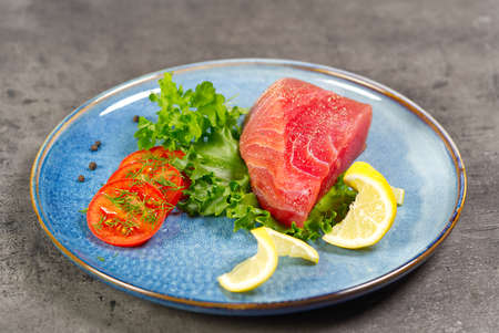 Raw tuna steak with salad and lemon on blue plate.