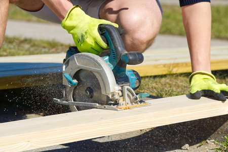 Carpenter working with a circular saw outside in sunny day. close-up