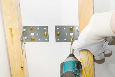 The master screws the metal corner to the concrete ceiling using a screwdriver