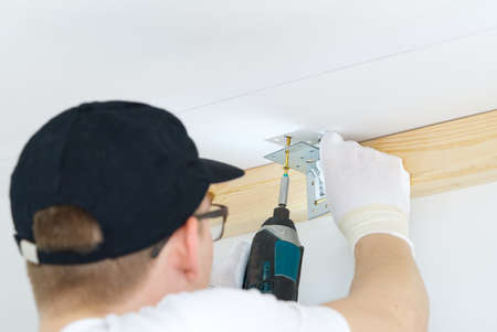 The master screws the metal corner to the concrete ceiling using a screwdriver