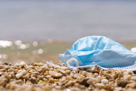 Used blue medical face mask lies on the beach. Environmental and coast plastic pollution during covid-19 pandemics. Pollution of seas and oceansの写真素材