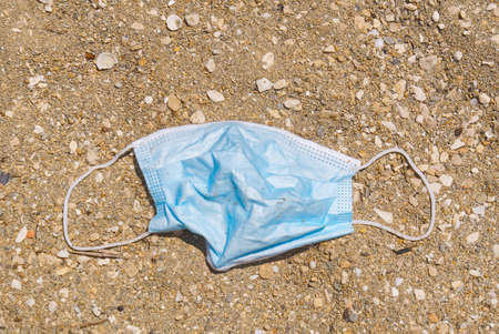 Used blue medical face mask lies on the beach. Environmental and coast plastic pollution during covid-19 pandemics. Pollution of seas and oceansの写真素材
