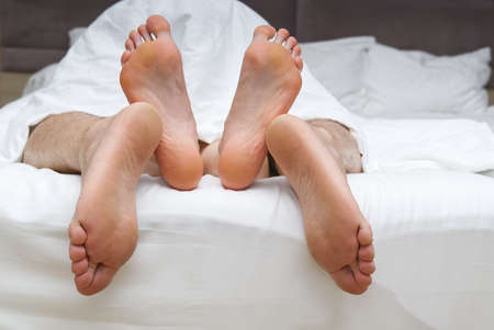 Lovers feet touch having sex on white linens in bedroom, sensual couple enjoy intimate moment relaxing in bed in man on top position. close-upの写真素材