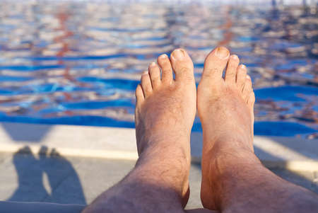 feet in front of blue water in open swimming pool in summer sunny dayの写真素材