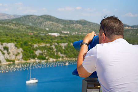 man using a panoramic telescope looking at the Mediterranean sea. Traveler exploring Adriatic sea...