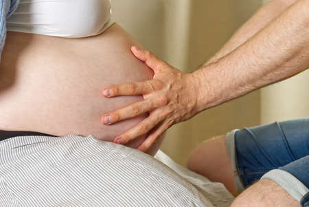 pregnant woman sits at home on the bed Pregnancy, motherhood, preparation and expectation concept. hands on belly of pregnant womanの写真素材