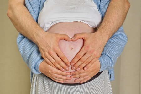 pregnant woman sits at home on the bed Pregnancy, motherhood, preparation and expectation concept. hands on belly of pregnant womanの写真素材