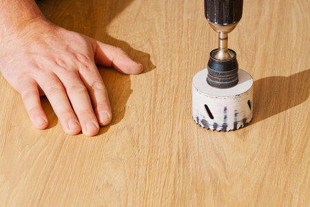 Worker with milling cutter in action at the workshop. Carpenter making holes in the wood board. Man uses drilling machine to make a hole on wooden plank. stock photoの写真素材