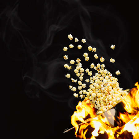 Flying popcorn on a dark background. Hot popcorn flying from pot under fire. cinema popcorn design...