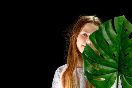Personal care, cosmetology concept for young teenagers. Portrait of young girl with healthy glow skin holds green monstera leaf and covers part of her face.の写真素材