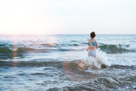 Swimming, traveling, playing with water. Girl in a swimsuit is playing on the beach with a sea wave...