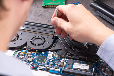Hands fixing motherboard of pc or laptop notebook close up in service. Laptop repair service. PC hardware upgrade and maintenance. Engineer fixing broken notebook.の写真素材
