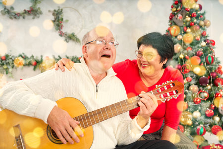 Father playing guitar during christmas. Happy man 60s playing guitar christmas songs. Happy christmas atmosphere.の写真素材