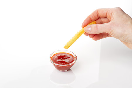 Hand dip french fries chips into ketchup isolated on white backgroundの写真素材