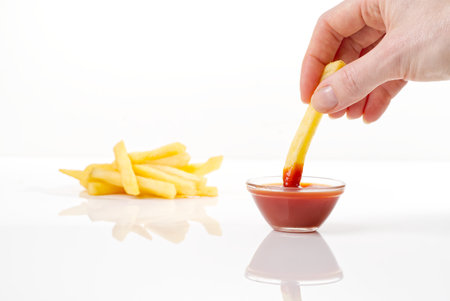 Hand dip french fries chips into ketchup isolated on white backgroundの写真素材