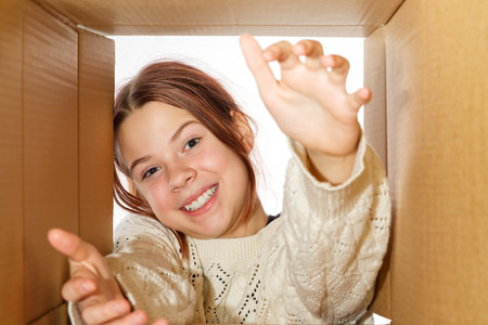 kid girl, teenager, unpacking and opening carton box, and looking inside with surprise.